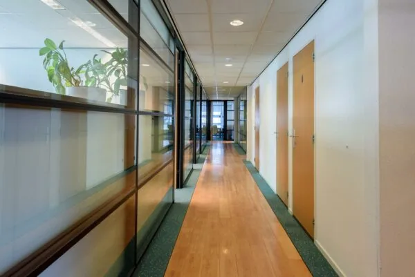 Gang in een modern kantoorpand aan de Rivium 2e Straat met glazen wanden en houten deuren.